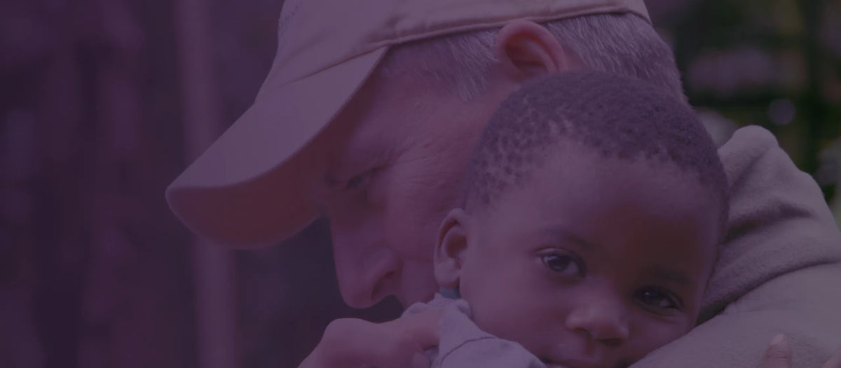 A close-up lifestyle shot of Dr. Meyer in a beige baseball cap holding a young child, with a solid purple overlay tinting the entire image.